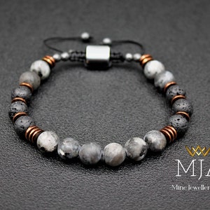May include: Adjustable bracelet with grey and white speckled stone beads, black lava beads, and copper-coloured spacers. The bracelet has a black cord and a silver-coloured clasp. The logo "MJA Mine Jewellery Art" is in the bottom right corner.