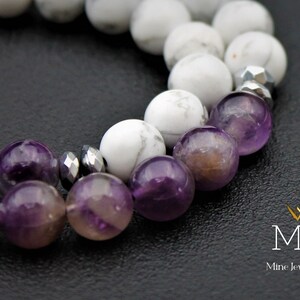 K&ouml;nnte beinhalten: Nahaufnahme eines Armbands aus wei&szlig;en und violetten Perlen. Das Armband besteht aus wei&szlig;en Howlith-Perlen und Amethyst-Perlen. Das Armband liegt auf einer schwarzen Oberfl&auml;che.