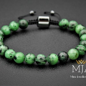 May include: A green gemstone bracelet with black flecks, featuring a silver adjustable clasp and black cord.