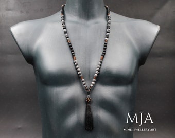 May include: A gray and black beaded necklace with a copper accent and a black tassel. The necklace is on a mannequin.