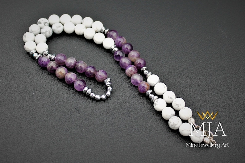 K&ouml;nnte beinhalten: Eine Halskette aus wei&szlig;en Howlith- und Amethyst-Edelsteinen mit silbernen Perlen. Die Halskette hat einen silbernen Verschluss und ist etwa 45 cm lang.