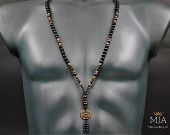 May include: A black and brown beaded necklace with a gold pendant featuring an eye design. The pendant is attached to a tassel of black beads. The necklace is displayed on a mannequin.
