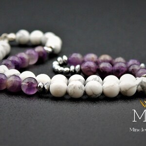 K&ouml;nnte beinhalten: Ein Armband aus wei&szlig;en und violetten Perlen. Das Armband besteht aus wei&szlig;en Howlith-Perlen und violetten Amethyst-Perlen. Das Armband hat einen silbernen Verschluss.