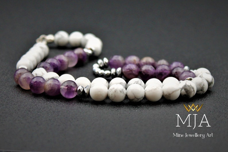 K&ouml;nnte beinhalten: Ein Armband aus wei&szlig;en und violetten Perlen. Das Armband besteht aus wei&szlig;en Howlith-Perlen und violetten Amethyst-Perlen. Das Armband hat einen silbernen Verschluss.