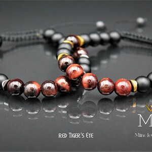 May include: Two bracelets with black onyx and red tiger's eye beads. The bracelets have gold accents and are tied with black cord. The text "RED TIGER'S EYE" and "MJA Mine Jewellery Art" is visible in the image.