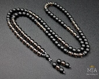 May include: A black and grey beaded necklace with a silver clasp. The necklace is made of two strands of beads, one black and one grey. The beads are round and have a matte finish.
