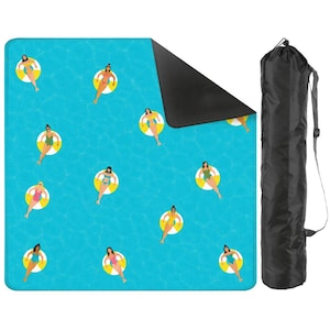 May include: A blue picnic blanket with a pattern of women in yellow and white inner tubes floating in water. The blanket is rolled up and stored in a black carrying bag with a shoulder strap. The blanket is rectangular.