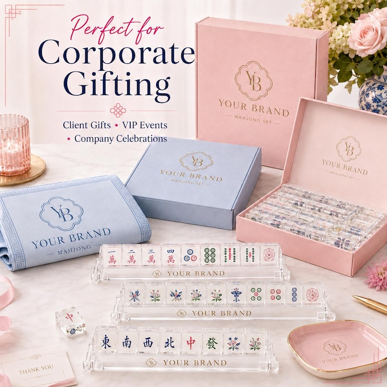 May include: A mahjong set featuring clear acrylic tiles with colorful symbols, three clear acrylic tile racks with the text YOUR BRAND, a light blue fabric mat, a pink storage box, and a pink tray, all branded with the YOUR BRAND logo.