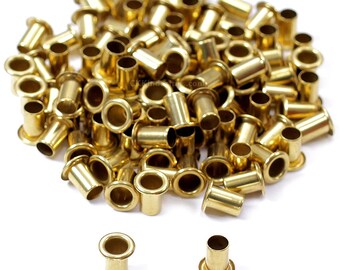 May include: A pile of shiny, brass-colored grommets. These small, cylindrical metal pieces have a flared base and a smooth, open center. They are used for reinforcing holes in fabric or other materials. The grommets are scattered on a white surface.