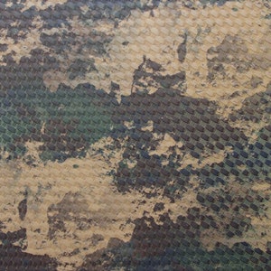 May include: A close-up of a camouflage pattern with a woven texture. The pattern is made up of shades of brown, green, and beige.