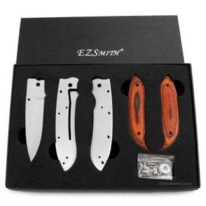 May include: A set of knife parts in a black box. The set includes a blade, handle scales, and hardware. The blade is made of stainless steel and has a satin finish. The handle scales are made of wood and have a natural finish. The hardware is made of stainless steel and includes screws, washers, and a pivot pin. The box is made of cardboard and has a black finish. The box has the text "EZSMITH" printed on the top.