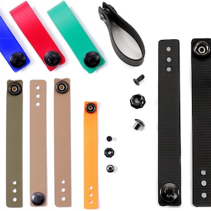 May include: An assortment of straps and fasteners in various colors. The image includes blue, red, and green straps, along with olive, tan, and orange straps. Black leather straps and metal hardware, including screws and snap fasteners, are also visible.
