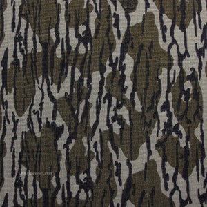 May include: A close-up of a camouflage fabric with a brown, black, and white pattern. The fabric has a textured weave.