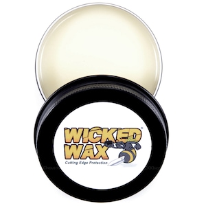 May include: A small, round tin container with a black lid and a white label. The label has the text "WICKED WAX" in yellow and black letters, with a cartoon bee and a knife. The text "Cutting Edge Protection" is also on the label.