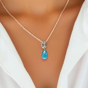 Könnte beinhalten: Eine silberne Halskette mit einem tropfenförmigen blauen Edelstein-Anhänger.