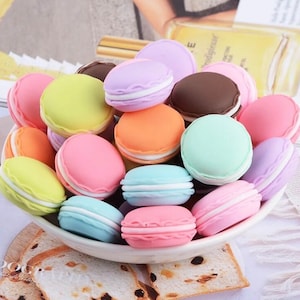 May include: A bowl filled with colorful macarons. The macarons are in various colors, including pink, blue, green, yellow, and brown. They are arranged in a random pattern.