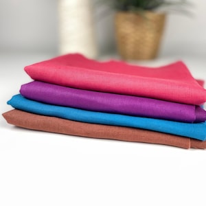 Può includere: Una pila di cinque campioni di tessuto colorati nelle tonalità del rosa, viola, blu e marrone. I tessuti sono ben piegati, mostrando le loro vibranti tonalità e trame. Ideale per progetti di artigianato o design tessile.