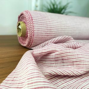 Può includere: Un rotolo di tessuto a righe rosa e bianche. Il tessuto è una miscela di lino e ha una texture sottile.