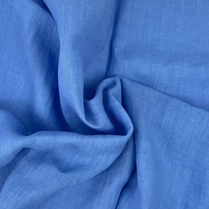 Può includere: Primo piano di un tessuto di lino blu con una trama testurizzata. Il tessuto è piegato e drappeggiato, mostrando la sua texture morbida e naturale.