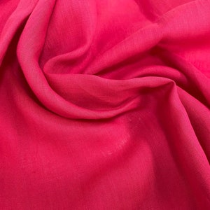 Può includere: Primo piano di un tessuto rosa acceso con una superficie liscia e leggermente testurizzata. Il tessuto è piegato e drappeggiato, mostrando la sua natura morbida e fluida.