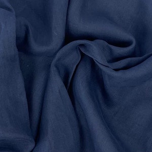 Può includere: Un primo piano di un tessuto di lino blu scuro con una trama testurizzata. Il tessuto è piegato e drappeggiato, mostrando la sua texture morbida e fluida.