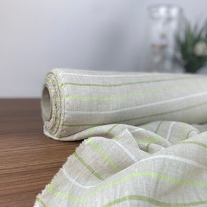 Può includere: Un rotolo di tessuto a righe bianche e verdi. Il tessuto è tessuto con una texture sottile e ha una sensazione leggera e ariosa.