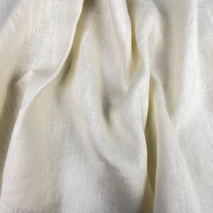 Può includere: Primo piano di un tessuto di lino color crema con pieghe morbide e una superficie strutturata. Il tessuto ha una lucentezza sottile e le pieghe creano ombre e riflessi, aggiungendo profondità. L'aspetto generale è naturale ed elegante.