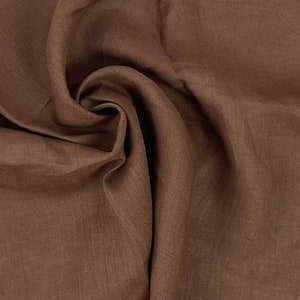 Può includere: Un primo piano di un tessuto di lino marrone con una trama testurizzata. Il tessuto è piegato e drappeggiato, mostrando la sua morbida e naturale consistenza.