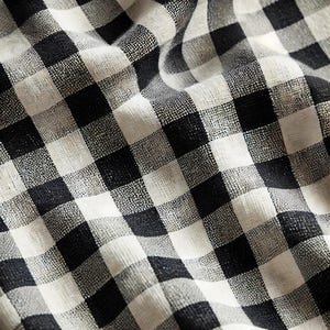 Può includere: Tessuto gingham bianco e nero con una trama tessuta. Il tessuto è piegato e mostra il motivo.
