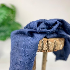 Könnte beinhalten: Ein blauer, strukturierter Stoff, der über einen Holzhocker gelegt ist. Der Stoff hat eine raue, unebene Oberfläche und einen leicht ausgefransten Rand.