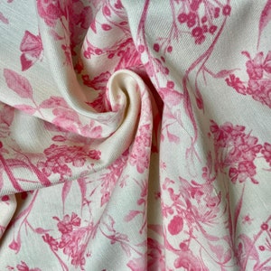 Op de afbeelding: Witte stof met een roze bloemenpatroon. De stof is zacht en heeft een subtiele textuur.