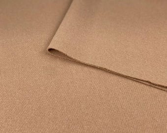 May include: Close-up of a brown fabric with a textured surface. The fabric is folded over itself, creating a soft, subtle drape.