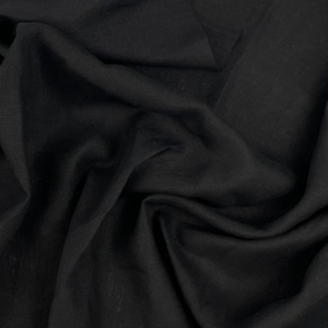 Può includere: Tessuto nero con una superficie liscia e leggermente strutturata. Il tessuto è drappeggiato e piegato, creando linee morbide e fluide.