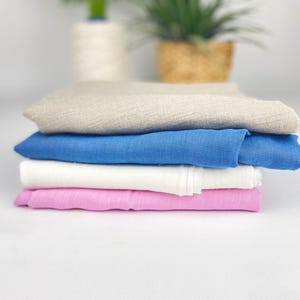 Può includere: Un set di quattro campioni di tessuto in diversi colori: beige, blu, bianco e rosa. Il tessuto è piegato e sembra morbido e liscio.