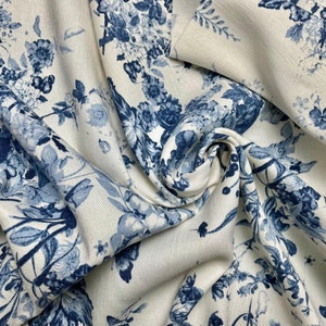 Può includere: Tessuto bianco con un motivo floreale blu. Il tessuto è piegato e drappeggiato, mostrando la trama e il dettaglio del design.