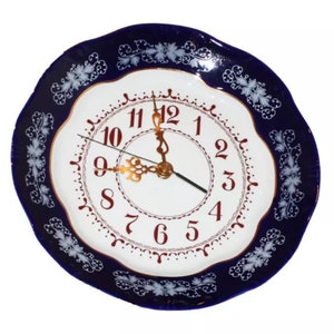 May include: A blue and white porcelain plate with a gold rim and a clock face in the center. The clock face has red numbers and gold hands.