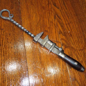 May include: A vintage adjustable wrench with a twisted metal handle and a wooden grip. The wrench is made of metal and has a silver finish. The handle is made of wood and has a dark brown finish.
