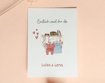 May include: A white card with the text "Endlich seid ihr da" and a watercolor illustration of two baby outfits hanging on a clothesline. The card also includes the names "Luisa & Lena".