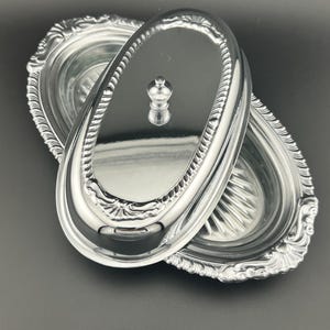 May include: A silver oval-shaped serving dish with a glass insert and a matching lid. The lid has a decorative knob on top.