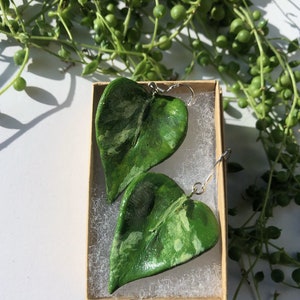 May include: A pair of green leaf-shaped earrings in a small brown box. The earrings are made of polymer clay and have a marbled green and white pattern.