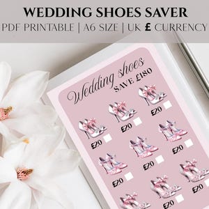 May include: A pink and white printable titled "WEDDING SHOES SAVER" with illustrations of high-heeled shoes. The text reads "SAVE £180". A silver pen rests on the white surface. White flowers are in the foreground.
