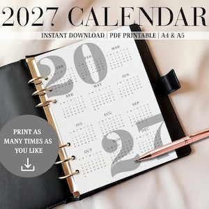 Könnte beinhalten: Eine Kalenderseite für 2027 mit weißem Hintergrund, großen grauen Zahlen und schwarzem Text für Monate und Daten. Der Kalender befindet sich in einem schwarzen Ordner mit goldenen Ringen und einem roségoldenen Stift. Der Text umfasst 2027 CALENDAR, INSTANT DOWNLOAD, PDF PRINTABLE, A4 & A5 sowie PRINT AS MANY TIMES AS YOU LIKE.