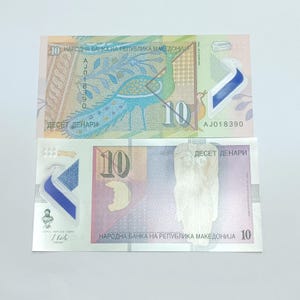 May include: Two Macedonian 10 Denar banknotes. The top bill features a peacock design in blue and green, with the text "ДЕСЕТ ДЕНАРИ". The bottom bill has a portrait and the text "НАРОДНА БАНКА НА РЕПУБЛИКА МАКЕДОНИЈА".