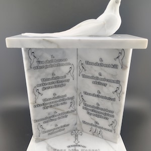 May include: A white marble sculpture featuring a dove perched atop a rectangular base. The base displays the Ten Commandments with angel illustrations. The text "EXODUS 20" and "Your Life Manual" are also visible.