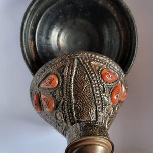 Op de afbeelding: Een decoratieve metalen container met een deksel, met ingewikkelde gravures en rode accenten. De container is gemaakt van koper en heeft een traditioneel ontwerp.
