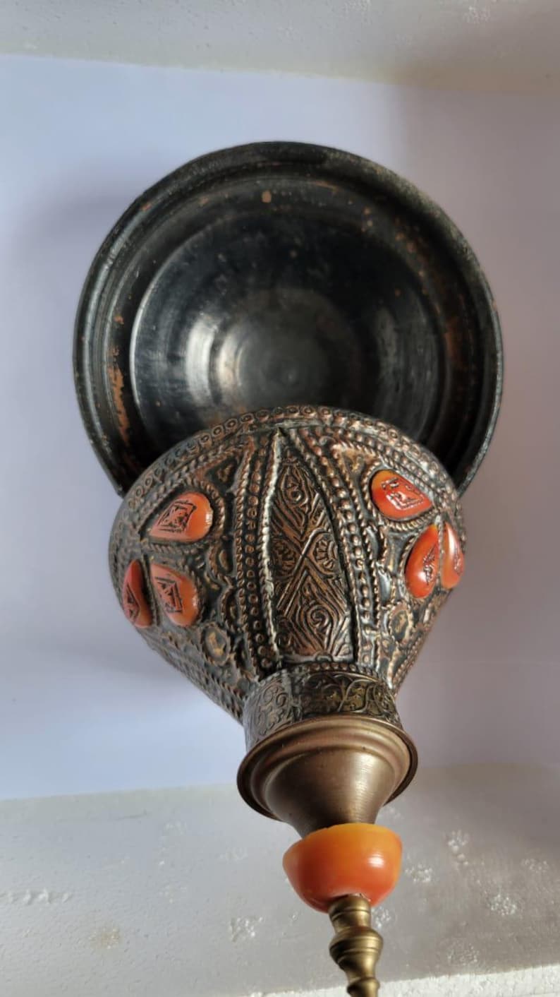 Op de afbeelding: Een decoratieve metalen container met een deksel, met ingewikkelde gravures en rode accenten. De container is gemaakt van koper en heeft een traditioneel ontwerp.