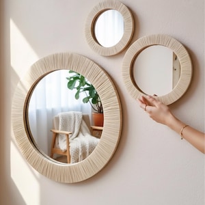 May include: Three circular wall mirrors with light beige, textured, wrapped frames. The mirrors vary in size, with one large mirror positioned on the left and two smaller mirrors arranged to the right, featuring reflective glass surfaces.