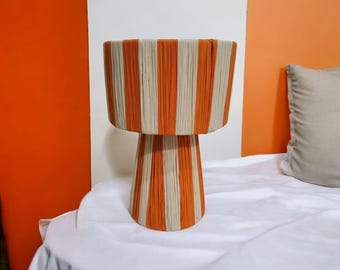 May include: A white and orange striped lamp with a round base. The lamp is made of woven material and has a modern design.