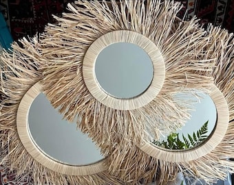 May include: Three round mirrors with natural woven raffia sunburst frames. The mirrors have a light beige color and a circular reflective surface. The raffia creates a textured, bohemian aesthetic, suitable for wall decor.