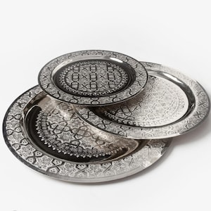May include: Three circular metal trays stacked on top of each other, each featuring a polished silver finish and a detailed black engraved geometric pattern consisting of interlocking stars and lines across the center and the wide rim.